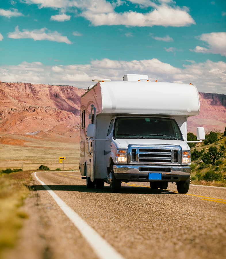 A moving white RV with the blue skies and clouds in the sky.